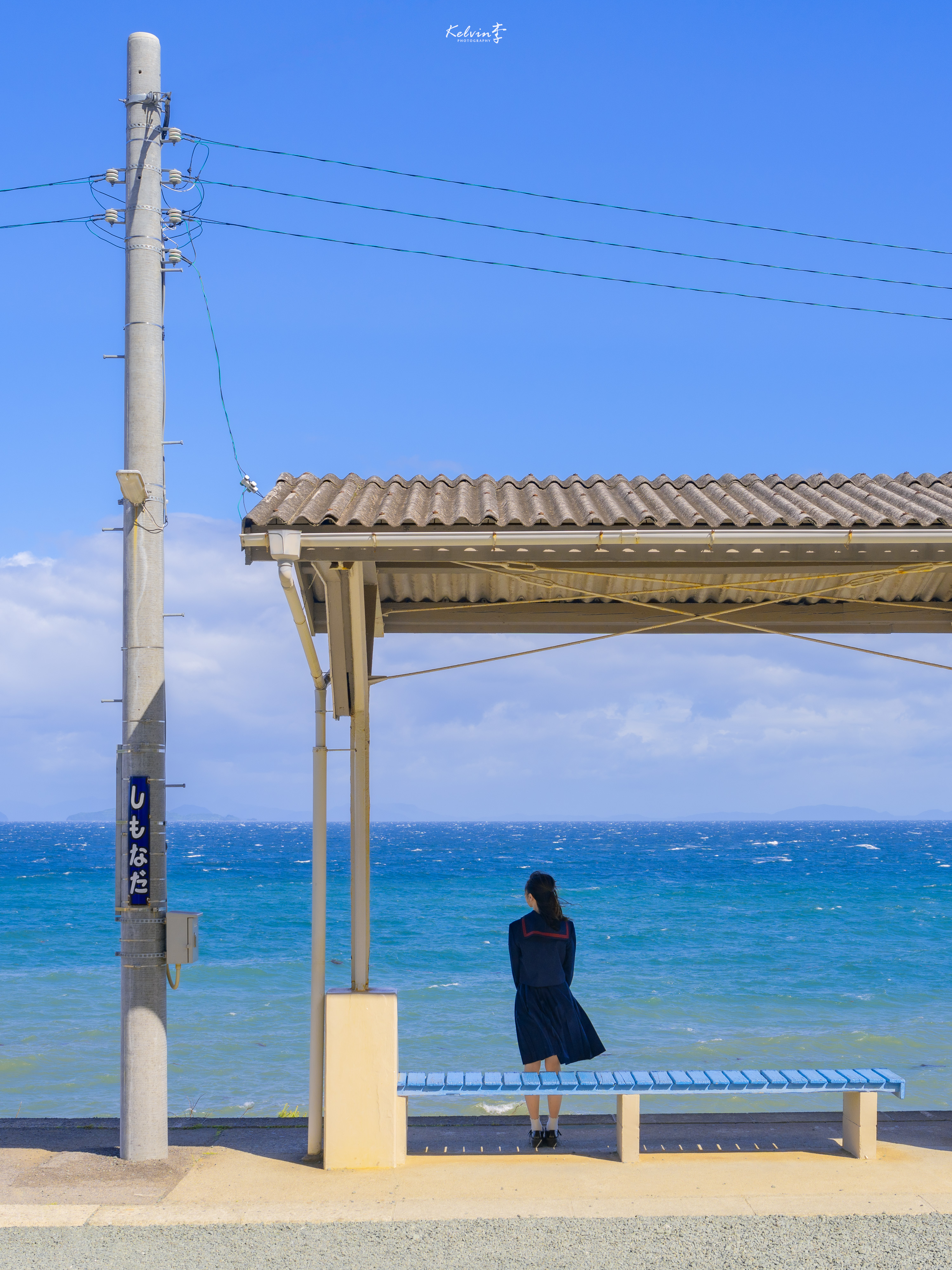 青い海を望む下灘駅のホームと、海を眺める人の後ろ姿。
